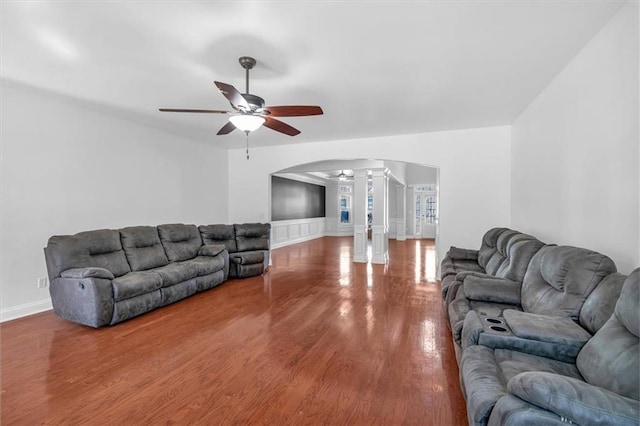 living area with arched walkways, ornate columns, ceiling fan, wood finished floors, and baseboards