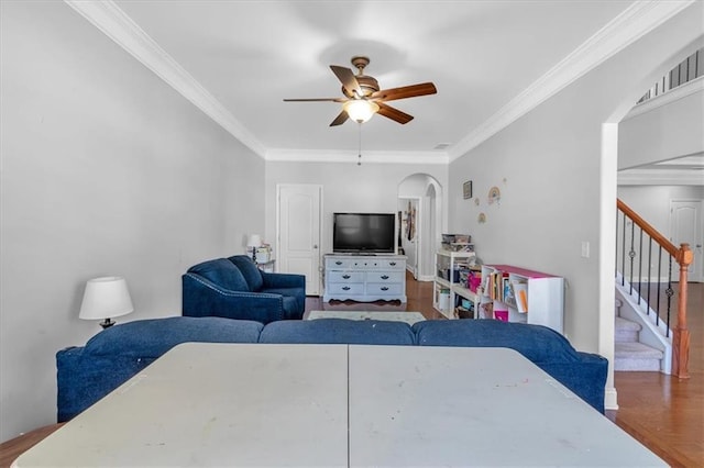 living room with arched walkways, a ceiling fan, ornamental molding, stairway, and wood finished floors