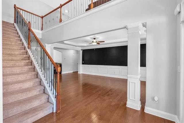 unfurnished living room with decorative columns, a ceiling fan, wood finished floors, stairs, and a decorative wall