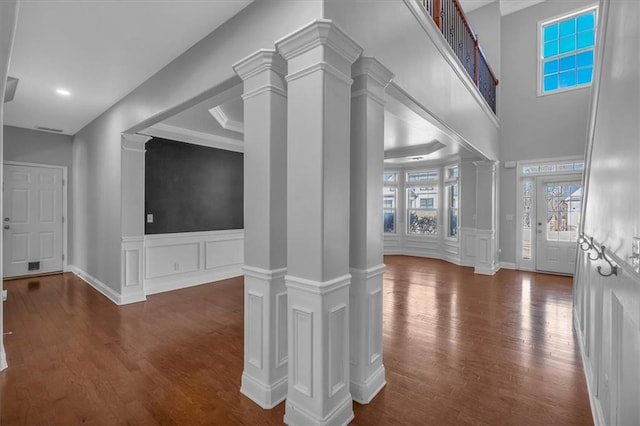 hall with ornate columns, wood finished floors, a decorative wall, and wainscoting