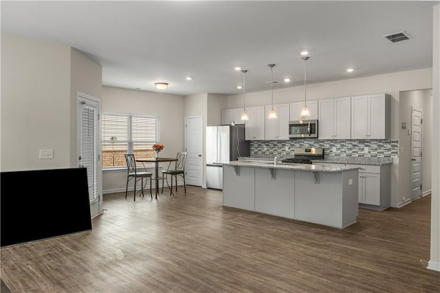 kitchen with decorative light fixtures, stainless steel appliances, light stone countertops, dark wood-type flooring, and a center island with sink