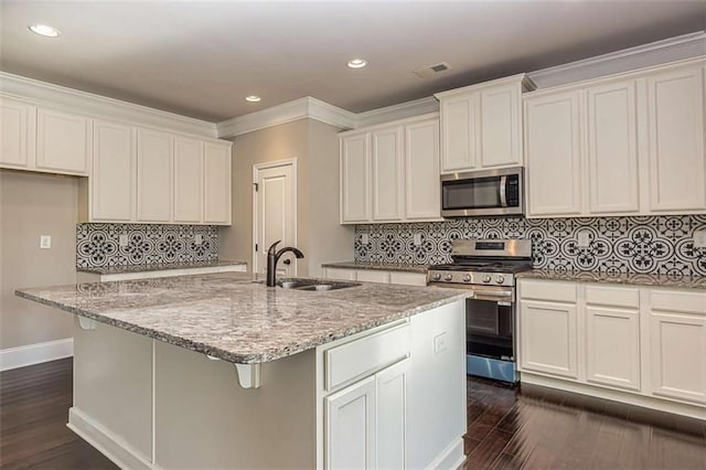 kitchen with a kitchen island with sink, a sink, stainless steel appliances, visible vents, and dark wood finished floors