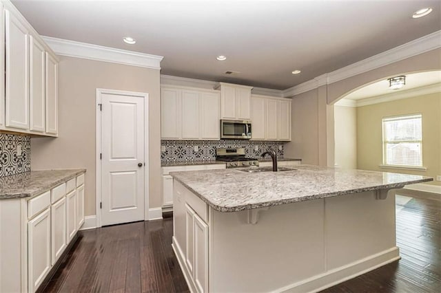 kitchen featuring a sink, appliances with stainless steel finishes, arched walkways, ornamental molding, and dark wood-type flooring