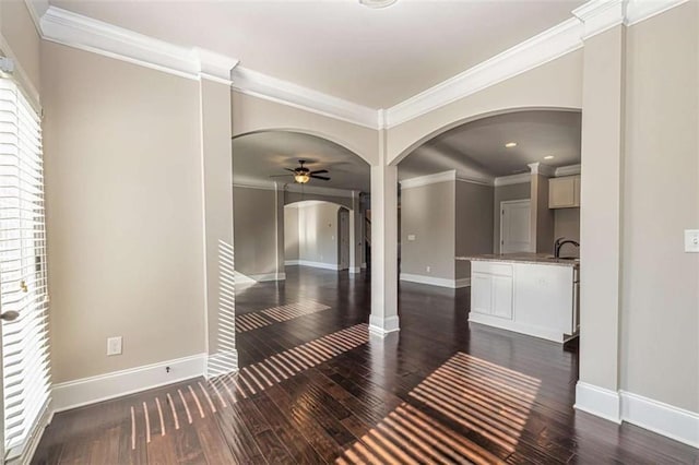 interior space featuring baseboards, ornamental molding, dark wood finished floors, and arched walkways