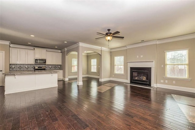 unfurnished living room featuring a wealth of natural light, dark wood-type flooring, and arched walkways