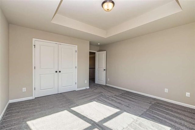unfurnished bedroom with a raised ceiling, baseboards, and carpet floors