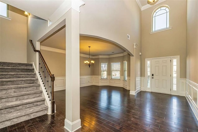 foyer with arched walkways, an inviting chandelier, a wainscoted wall, dark wood-style flooring, and crown molding