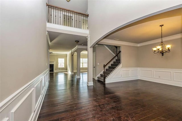 foyer entrance featuring hardwood / wood-style flooring, stairway, arched walkways, ornamental molding, and a decorative wall