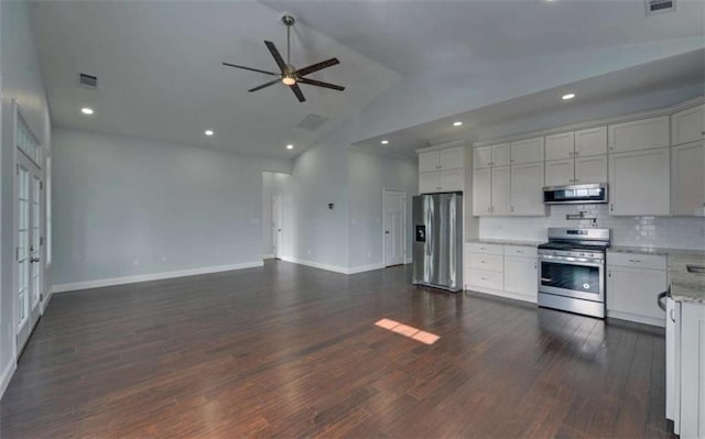 kitchen with appliances with stainless steel finishes, lofted ceiling, backsplash, light stone counters, and dark wood-type flooring