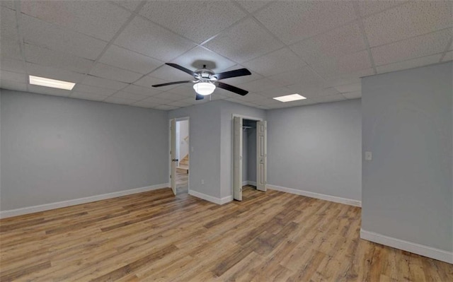 basement with a paneled ceiling, light hardwood / wood-style floors, and ceiling fan