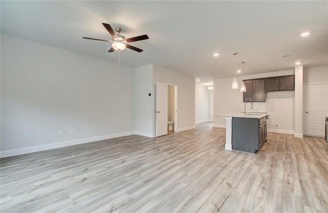 kitchen with ceiling fan, sink, light hardwood / wood-style flooring, hanging light fixtures, and a kitchen island with sink