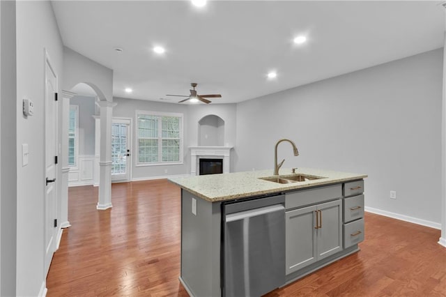 kitchen with a center island with sink, decorative columns, gray cabinetry, a sink, and dishwasher