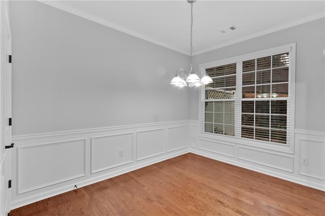 unfurnished dining area with visible vents, wainscoting, ornamental molding, wood finished floors, and an inviting chandelier