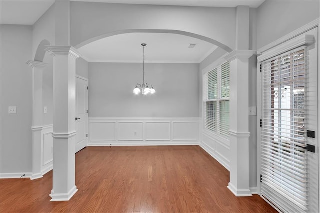 unfurnished dining area featuring visible vents, wainscoting, wood finished floors, ornate columns, and a notable chandelier