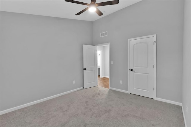 unfurnished bedroom featuring lofted ceiling, light colored carpet, visible vents, a ceiling fan, and baseboards