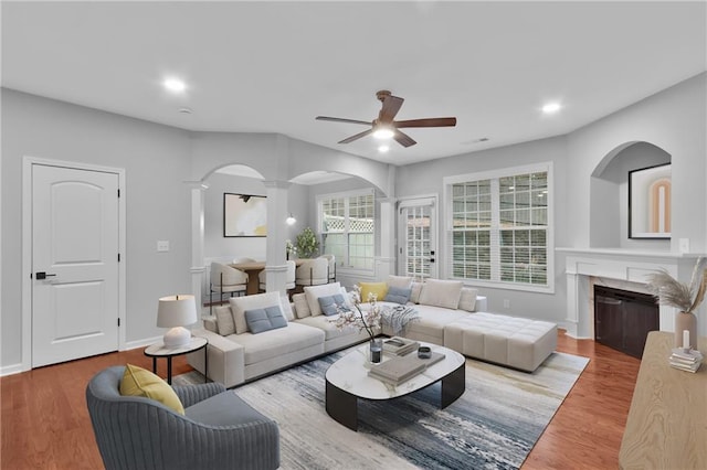 living area featuring arched walkways, a fireplace, recessed lighting, wood finished floors, and baseboards