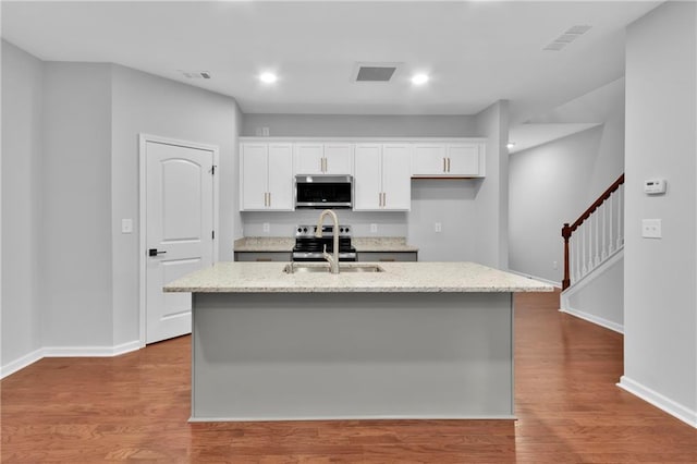 kitchen featuring a center island with sink, appliances with stainless steel finishes, white cabinetry, a sink, and light wood-type flooring