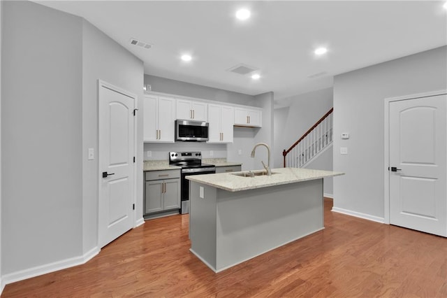 kitchen featuring light wood finished floors, a center island with sink, appliances with stainless steel finishes, a sink, and recessed lighting