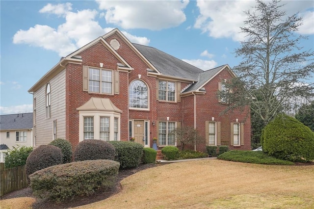 view of front facade with brick siding, a front lawn, and fence