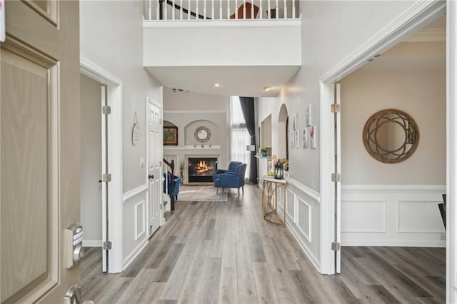 entrance foyer with wood finished floors, arched walkways, a lit fireplace, wainscoting, and a decorative wall