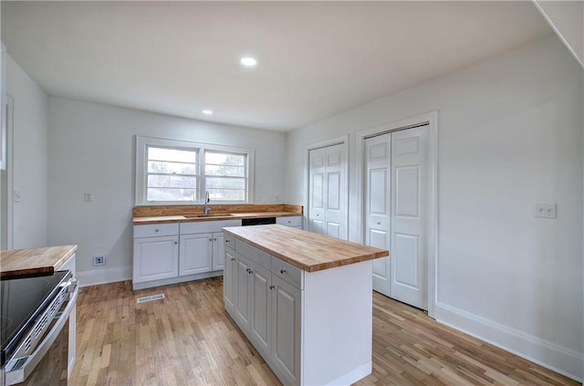 kitchen featuring wooden counters, a kitchen island, sink, range, and white cabinetry