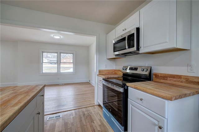 kitchen featuring white cabinets, stainless steel appliances, butcher block counters, and light hardwood / wood-style floors