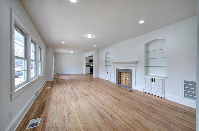 unfurnished living room featuring built in shelves and light hardwood / wood-style floors