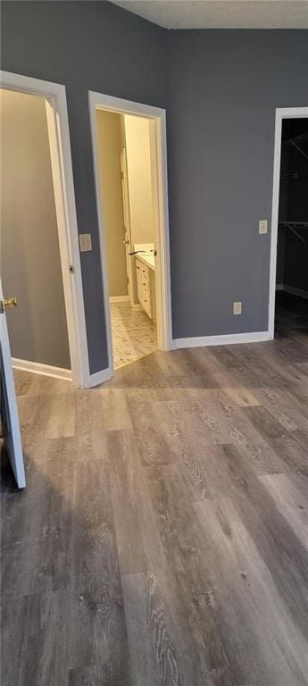 unfurnished bedroom with a spacious closet, ensuite bath, a closet, and hardwood / wood-style flooring