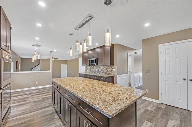 kitchen featuring stainless steel appliances, light wood-style floors, decorative backsplash, and dark brown cabinets