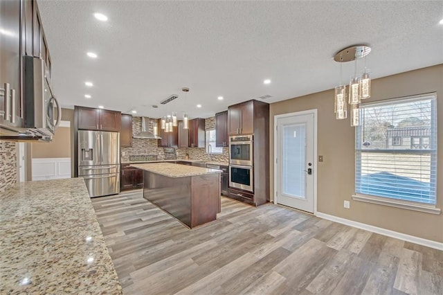 kitchen with plenty of natural light, tasteful backsplash, wall chimney exhaust hood, appliances with stainless steel finishes, and light wood-type flooring