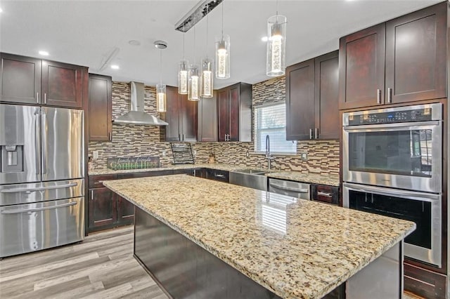 kitchen with light wood finished floors, stainless steel appliances, backsplash, a sink, and wall chimney range hood