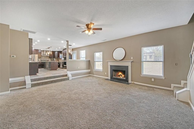 unfurnished living room featuring visible vents, baseboards, light colored carpet, ceiling fan, and a textured ceiling