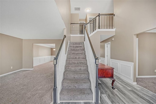 staircase with a decorative wall, a wainscoted wall, wood finished floors, carpet flooring, and visible vents