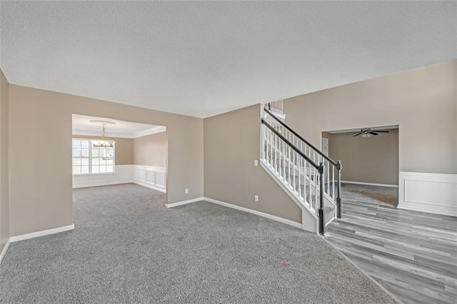 unfurnished living room featuring a wainscoted wall, stairs, a decorative wall, and a textured ceiling