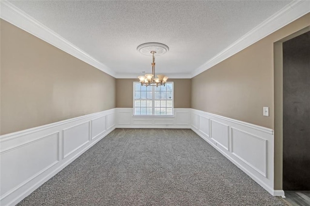 carpeted spare room with a wainscoted wall, crown molding, a chandelier, and a textured ceiling