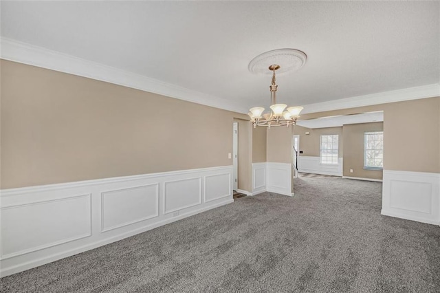 spare room with a chandelier, wainscoting, crown molding, and carpet flooring