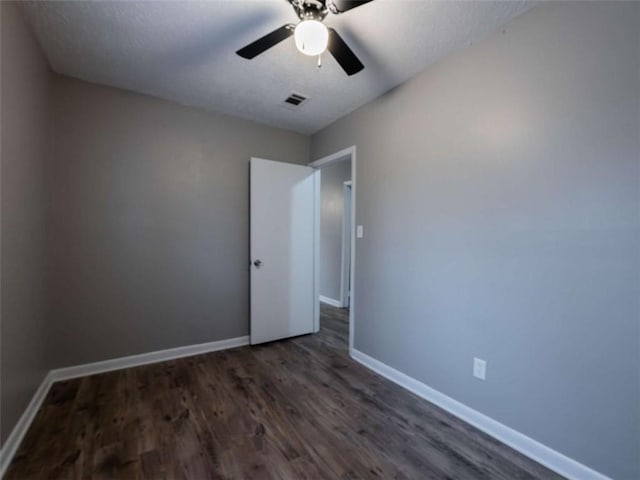 spare room with dark wood-style flooring, visible vents, ceiling fan, and baseboards