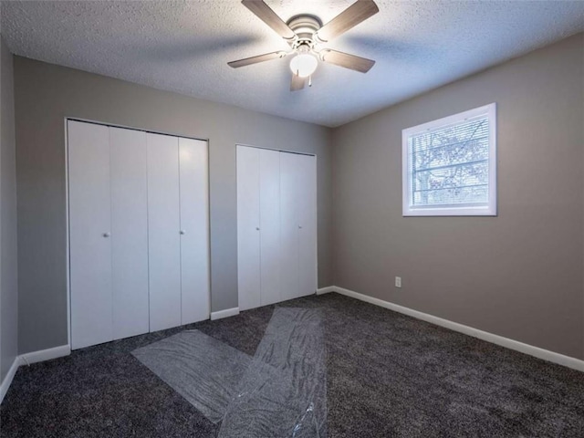 unfurnished bedroom featuring multiple closets, dark colored carpet, and a textured ceiling