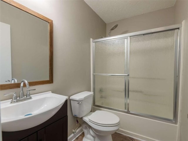 bathroom featuring a textured ceiling, toilet, shower / bath combination with glass door, and vanity