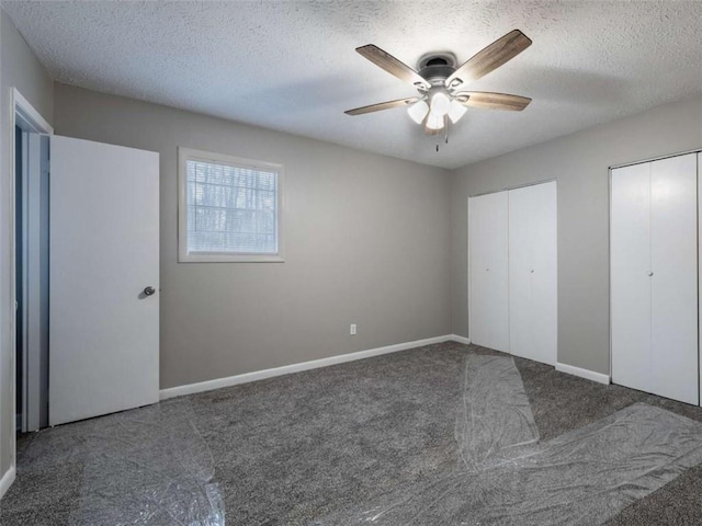 unfurnished bedroom featuring baseboards, a ceiling fan, a textured ceiling, carpet flooring, and two closets