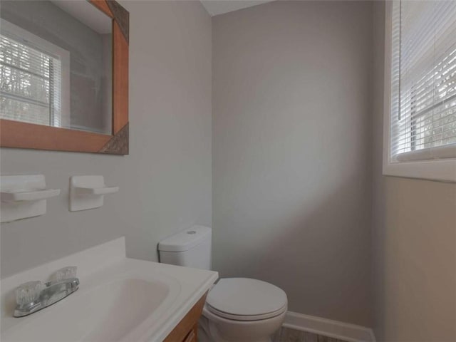 half bathroom with vanity, toilet, and baseboards