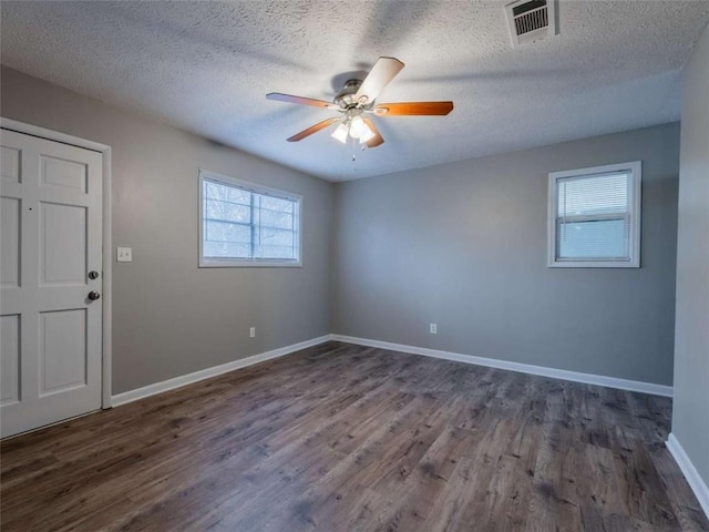 empty room with baseboards, visible vents, a ceiling fan, dark wood-type flooring, and a textured ceiling