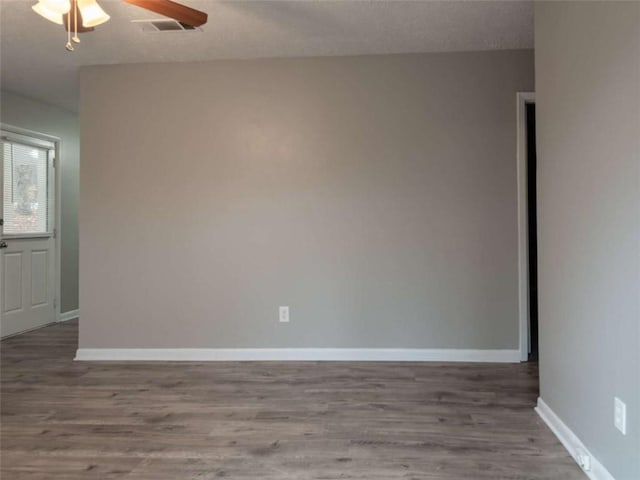 empty room with a textured ceiling, wood finished floors, visible vents, a ceiling fan, and baseboards