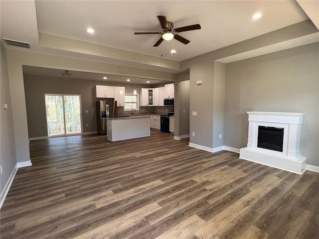 unfurnished living room featuring dark wood-style floors, baseboards, and a ceiling fan