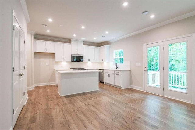 kitchen featuring stainless steel appliances, a sink, backsplash, a kitchen island, and light wood-style floors