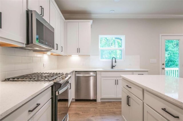 kitchen with sink, white cabinets, appliances with stainless steel finishes, light stone counters, and light hardwood / wood-style floors