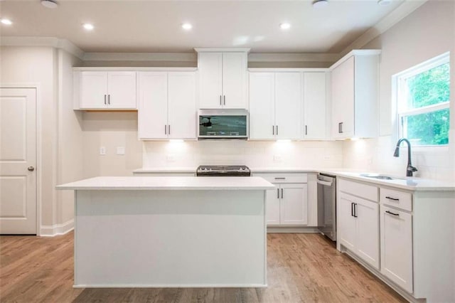 kitchen with appliances with stainless steel finishes, a sink, a center island, white cabinetry, and light countertops