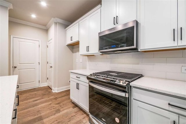 kitchen featuring stainless steel appliances, light wood finished floors, white cabinets, ornamental molding, and baseboards