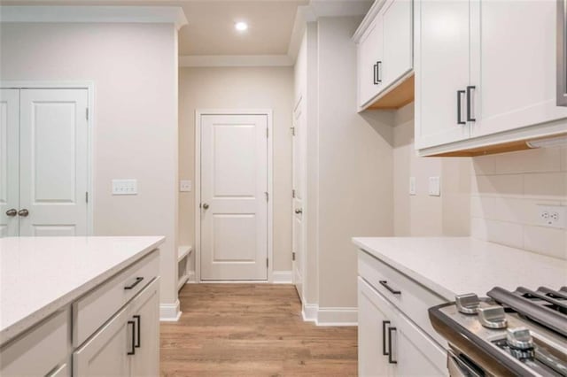 kitchen featuring light wood finished floors, backsplash, white cabinetry, stove, and baseboards