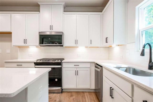 kitchen featuring appliances with stainless steel finishes, a sink, white cabinetry, light wood-style floors, and decorative backsplash